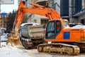 A large crawler excavator and a truck are clearing snow from the carriageway of a city street Royalty Free Stock Photo