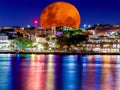 Large orange full blood moon rising behind Sydney CBD buildings NSW Australia neon lights reflecting on the harbou harbour