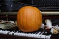 A large orange pumpkin stands on the keys of an old piano next to dry ears of yellow corn Royalty Free Stock Photo