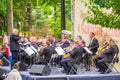 a large orchestra plays music in a city park on a summer day