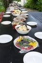 large outdoor festive table. dishes with food are covered with plastic wrap