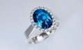 The large oval blue diamond is surrounded by many diamonds on the ring made of platinum gold placed on a white background. 3d