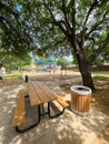 Large picnic table with trash can under mature oak tree shade, drinking water fountain near playground climbing structure Royalty Free Stock Photo