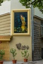 A large picture in the frame with a painted girl on the wall of the house with an inscription cafe under it. And