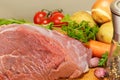 A large piece of raw pork is surrounded by several vegetables Royalty Free Stock Photo