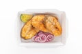 Large pieces of fried fish - pike perch with herbs, red onion and lemon in a disposable paper box on a white background. Royalty Free Stock Photo