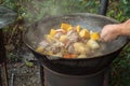 Large pieces of meat, ears of corn, potatoes and vegetables are fried in a cast-iron cauldron on an outdoor wood-burning stove. Royalty Free Stock Photo