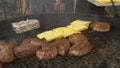 Large pieces of meat are fried on a large round grill, the cook lays penciled pita bread on the grill