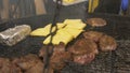 Large pieces of meat are fried on a large round grill, the cook lays penciled pita bread on the grill