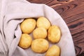 A large pile of fresh, hard young potatoes on a gray bag and on a wooden table. Uncooked and organic new light brown potatoes. Royalty Free Stock Photo