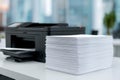 Large pile of freshly printed white sheets stacked on a desk next to a black multifunction office printer in a modern workspace Royalty Free Stock Photo