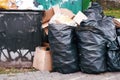 Large pile of household rubbish in black plastic bags near a dumpster in a big city