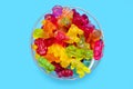 A large pile of multi-colored jelly gummy candies in a glass bowl on a blue background Royalty Free Stock Photo