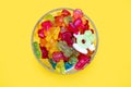 A large pile of multi-colored jelly gummy candies in a glass bowl on a yellow background Royalty Free Stock Photo