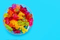 A large pile of multi-colored jelly marmalade candies in a glass bowl on a blue background Royalty Free Stock Photo