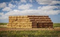 Large pile of square bales of hay or straw are piled high at the edge of a plowed field with flat horizon and blue sky with fluffy Royalty Free Stock Photo