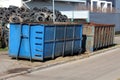 Large pile of used car tyres behind two heavily used industrial partially rusted strong blue metal recycling containers Royalty Free Stock Photo