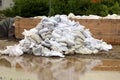 Large pile of white sandbags used for flood protection waiting to be removed after flood surrounded with muddy water and wooden