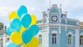 A large pile of yellow and blue helium balloons against the sky and a house with a clock in the background Royalty Free Stock Photo