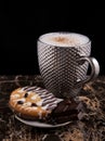 Large pimpled silver cup of coffee and cakes bisquits chocolate and coffee beans on the granite surface and black Royalty Free Stock Photo