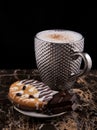 Large pimpled silver cup of coffee and cakes bisquits chocolate and coffee beans on the granite surface and black
