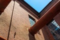 Large pipe emerging from a brick wall on the inside corner of an industrial complex building, windows and blue sky