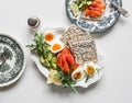 A large plate of breakfast, brunch, snack - boiled eggs, avocado, lightly salted salmon, bread, arugula on a light background, top