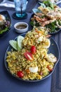 A large plate of seafood pineapple fried rice looks delicious on a porcelain plate. On a table in a restaurant There are other