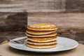 A large plate stack of pancakes with a fork against a wood background plain with no syrup