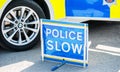 Large Police Slow sign on the road beside a patrol vehicle.