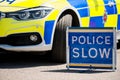 Large Police Slow sign on the road beside a patrol vehicle.