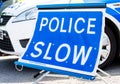 Large Police Slow sign on the road beside a patrol vehicle.