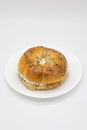 Large Poppy Seed Bagel filled with Cream Cheese on a White Plate with a White Background Royalty Free Stock Photo