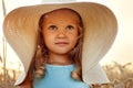A large portrait of a child against the background of rye ears. A little blonde girl in a blue dress and a very big mother`s hat