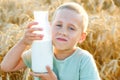 Large portrait of a child with milk on a background of wheat. The boy holds a glass bottle to his face. Picnic at sunset on a