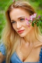 A large portrait of a girl with a pink cherry blossom flower near her face in a park. A blonde girl in a blue sundress enjoys