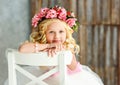 Large portrait of lovely cute little girl - blonde in a wreath of live roses in a white beautiful dress in a bright studio. Close- Royalty Free Stock Photo