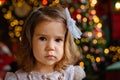 A large portrait of a sad little girl on the background of a beautifully decorated Christmas tree with red-green balls and bokeh Royalty Free Stock Photo