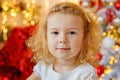 A large portrait of a small curly blonde girl against the background of bokeh lights and a decorated Christmas tree Royalty Free Stock Photo