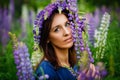 Large portrait of a woman in a wreath on a lupine field. A meadow of purple flowers in summer. A girl with long hair holds a