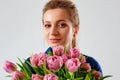 A large portrait of a young woman on a gray background with a large bouquet of pink tulips near her face. The concept of a spring