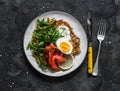 Large potato rosti with egg, arugula, salmon and Greek yogurt sauce on a dark background, top view. Delicious food