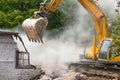 Large powerful yellow excavator destroys an old dilapidated house