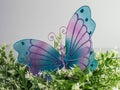 Large purple and blue mesh butterfly with glitter and gems on top of a white and green plant with a white background. Perfect for