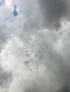 Large rain drop splattered on window looking up at a clouded sky