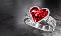 The large red diamond heart shape is surrounded by many diamonds on the ring made of platinum gold placed on a gray background. Royalty Free Stock Photo