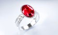 The large red diamond or ruby is surrounded by many diamonds on the ring made of platinum gold placed on a gray background.