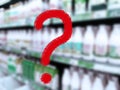 Large red question mark on abstract blur image of supermarket background. Defocused shelves with dairy products. Grocery store. Royalty Free Stock Photo