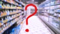 Large red question mark on abstract blur image of supermarket background. Defocused shelves with food and product. Grocery