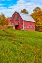 Large red vintage country barn in grassy fields with fall trees behind Royalty Free Stock Photo